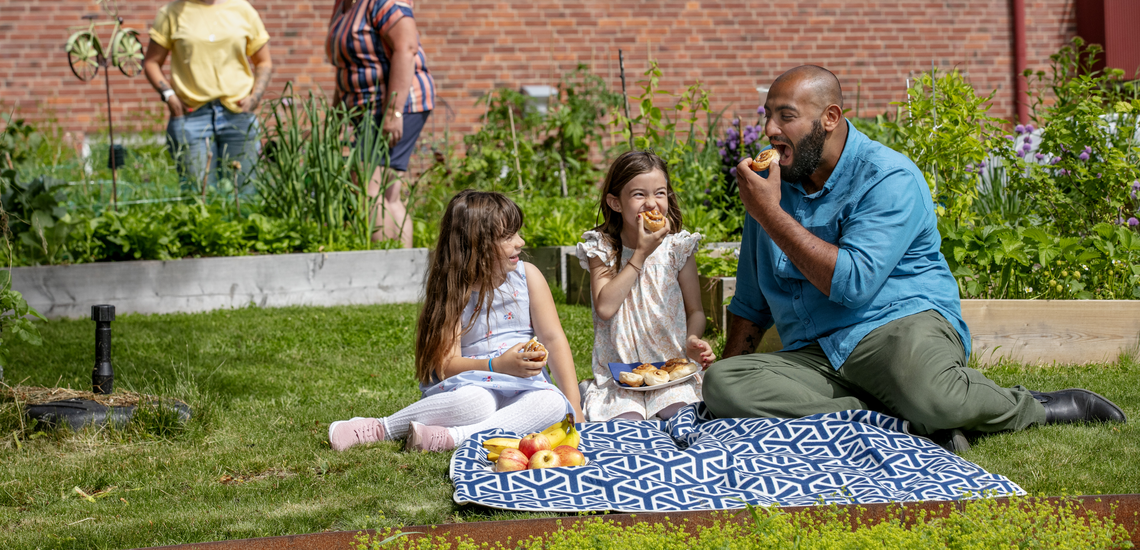 Pappa och döttrar har picnic med bullar en solig sommardag.