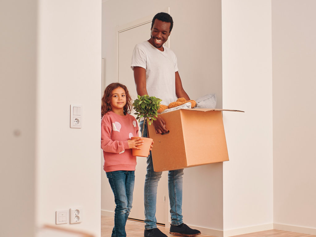 Bild på en pappa och dotter som flyttar lådor i en tom lägenhet.