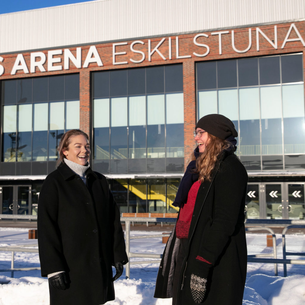 Två studenter skrattar tillsammans framför STIGA Sports Arena.