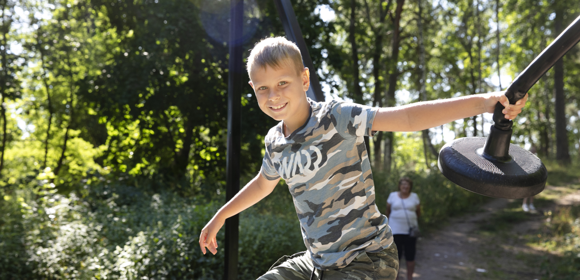 Ett barn leker på en äventyrsbana omgiven av grönskande skog