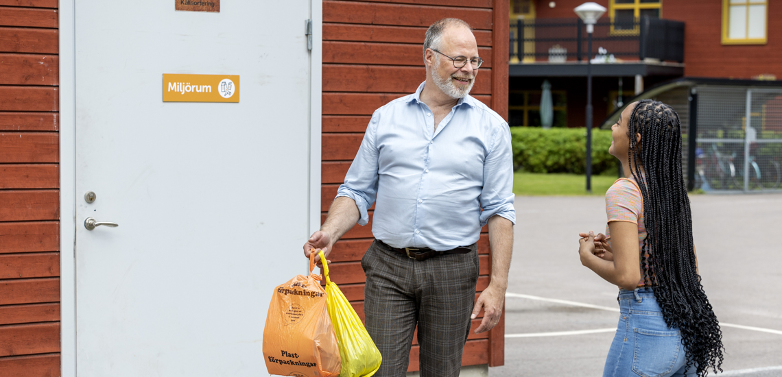 Man och kvinna framför ett miljöhus. Mannen har två soppåsar i handen.