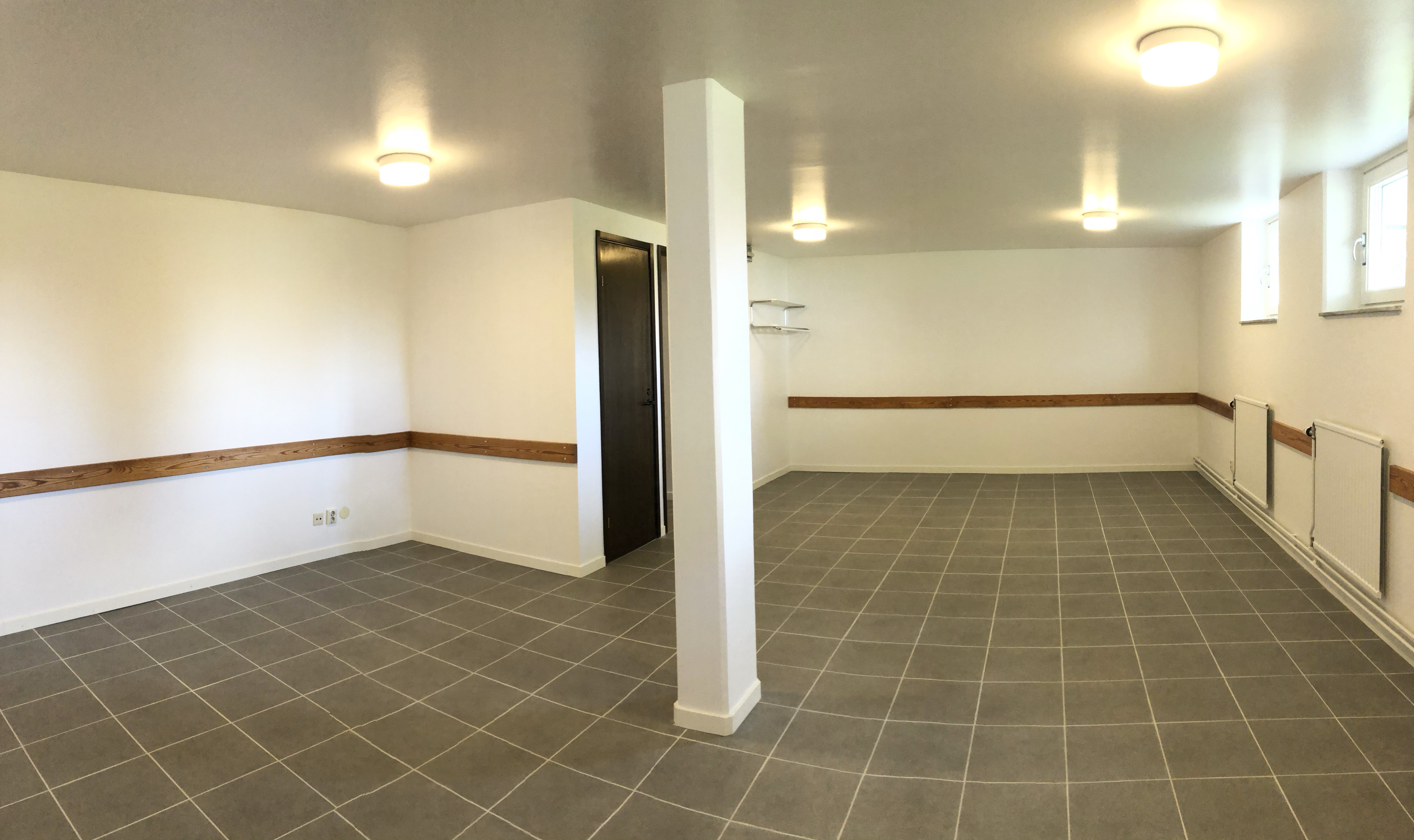 Rum med ljusa väggar och grått golv. Två källarfönster.