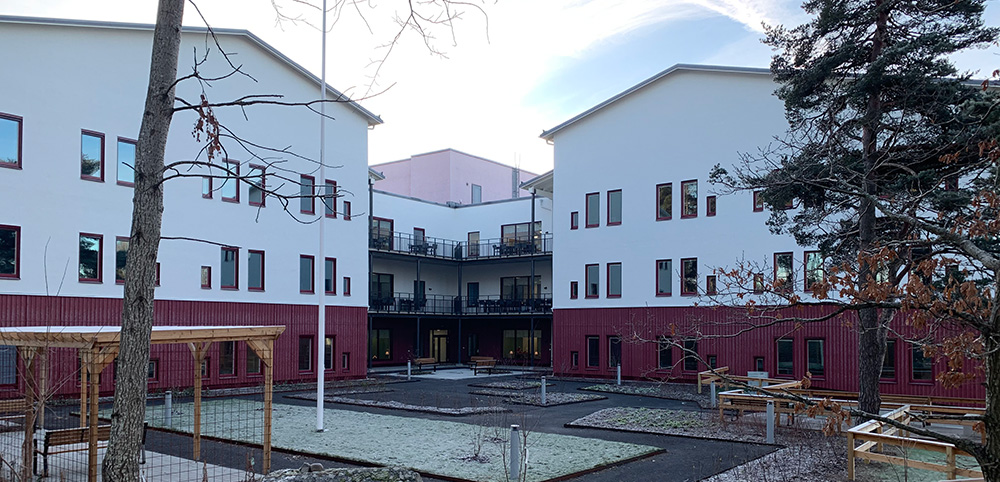 Vågens vård- och omsorgsboende, två byggnader med tre våningar vardera. Tallar och promenadstråk i förgrunden.