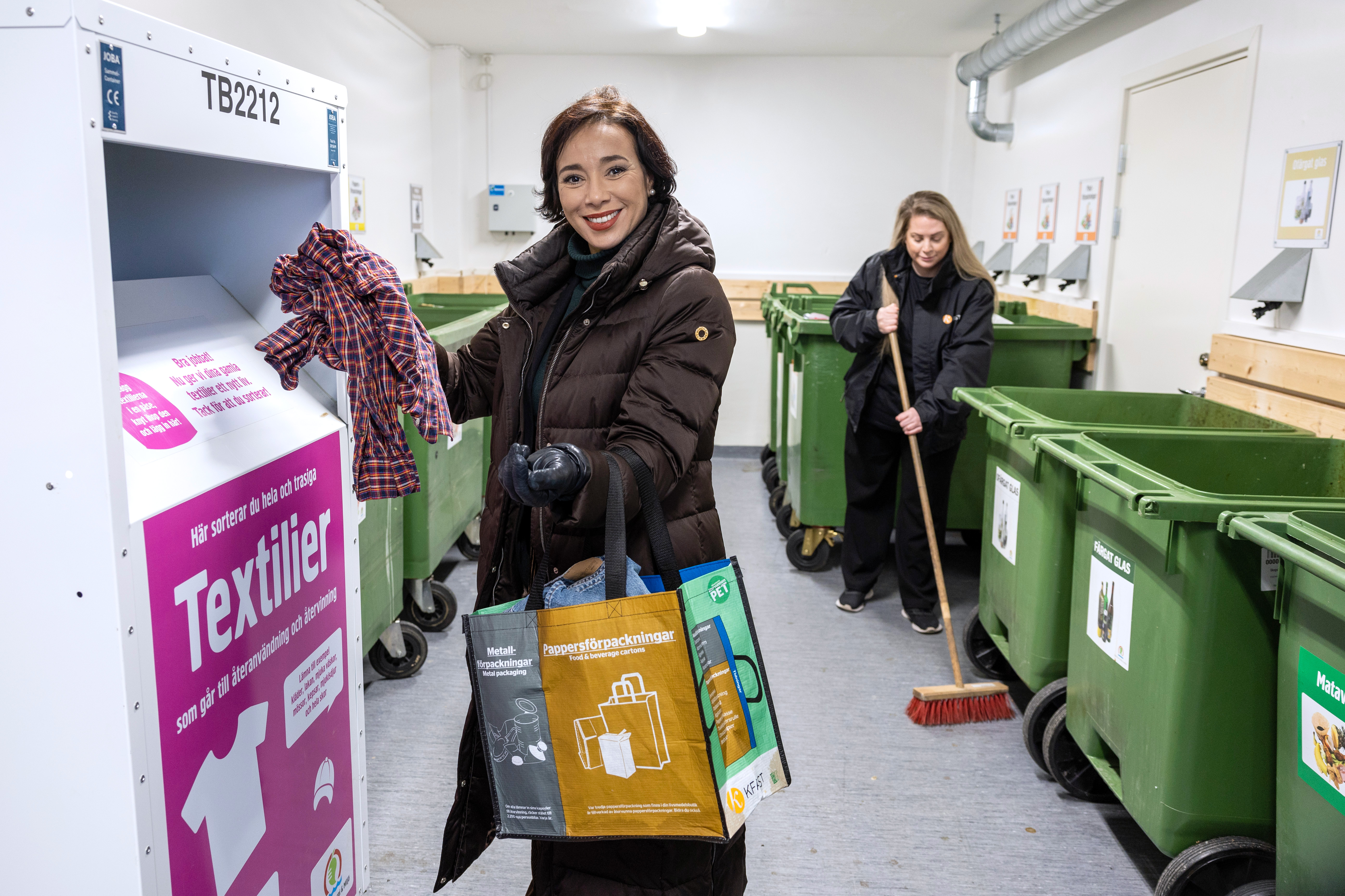 Kvinna sorterar kläder och fastighetsskötare sopar i miljöhus.