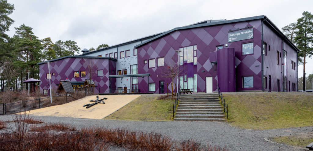 Lilamönstrad förskolebyggnad i två vångar, omgärdad av gräsmatta