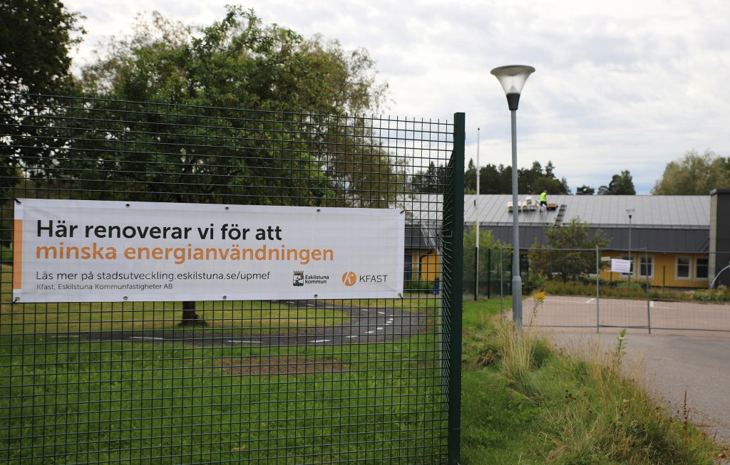 Staket runt förskola med skylt med texten Här renoverar vi för att minska energiförbrukningen.