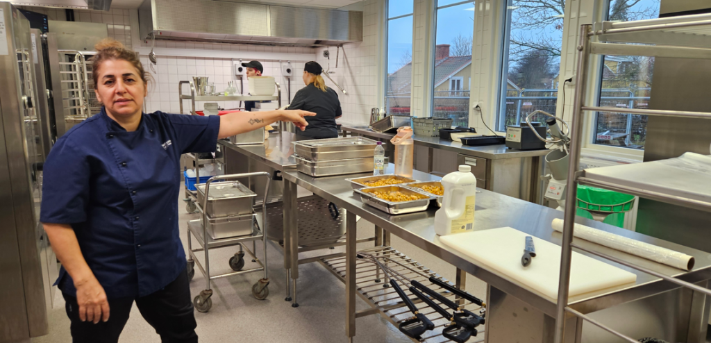 Kvinna står i skolkök och pekar på tillagningsytor i köket.