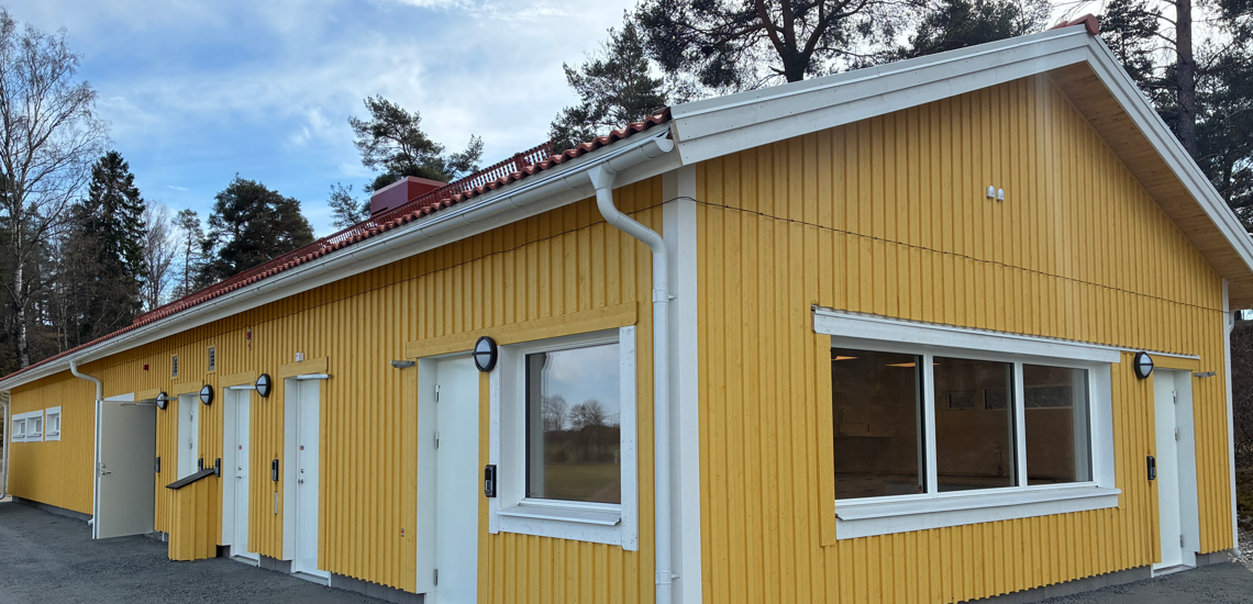 En gul byggnad med vita fönster och rött tak.