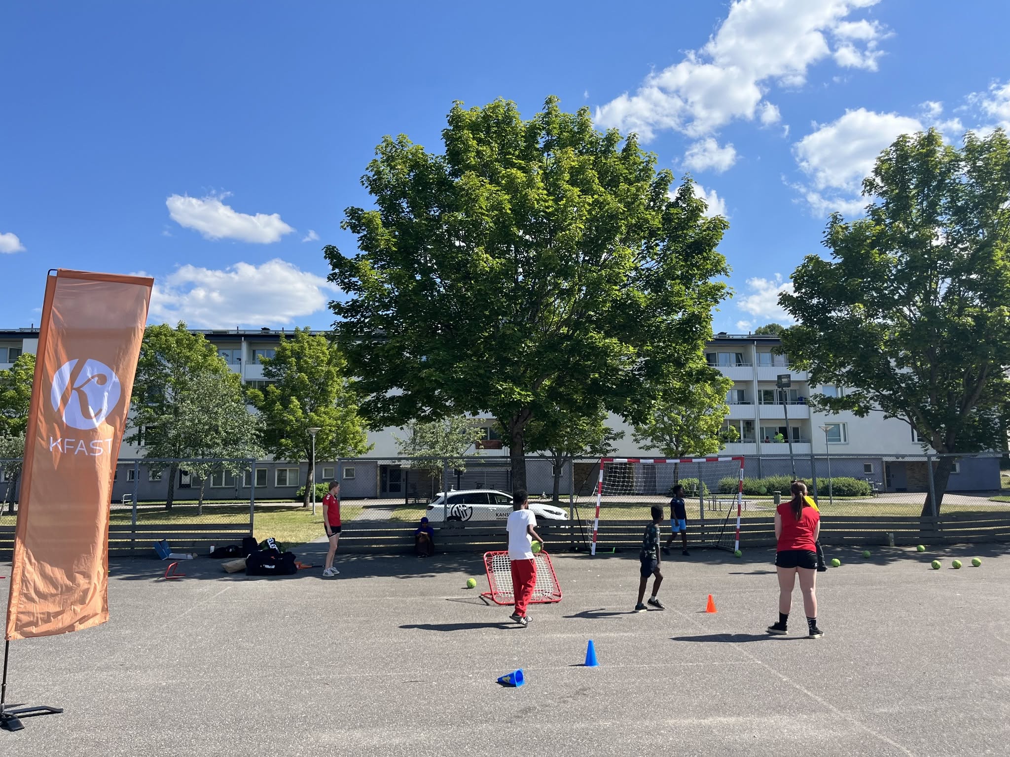 Barn och ungdomar spelar handboll utomhus i ett bostadsområde.