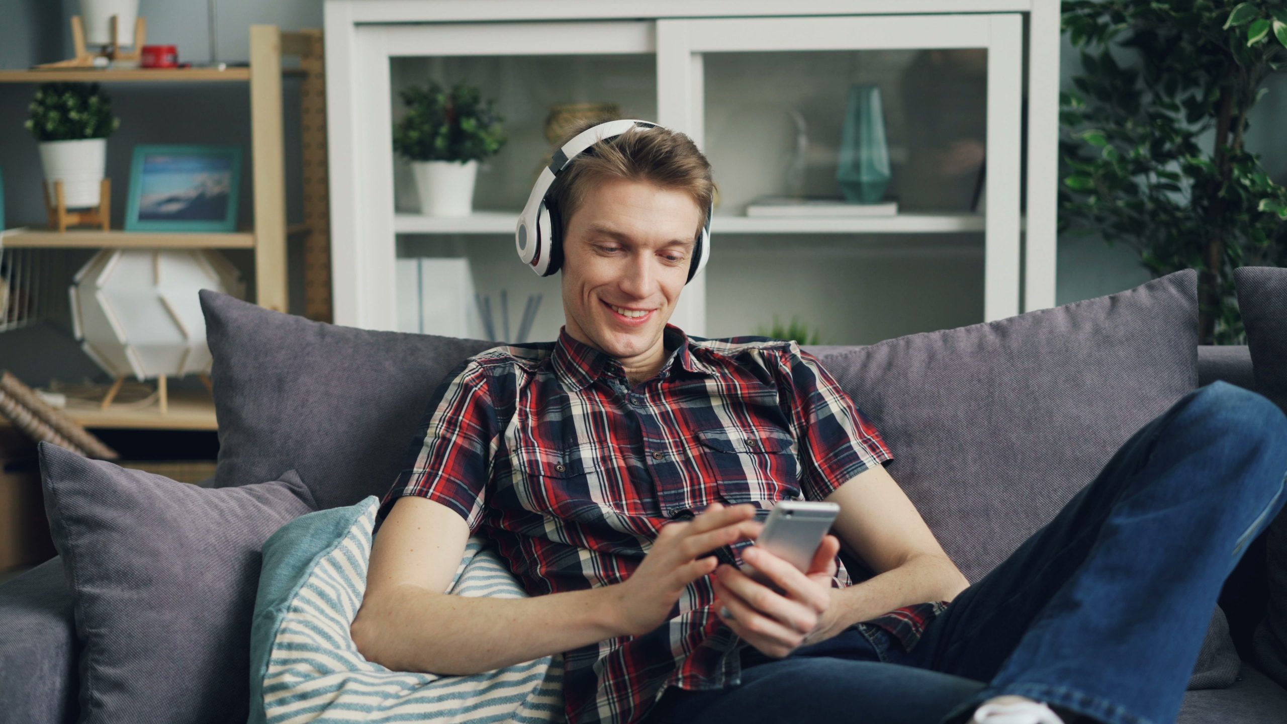 Ung kille sitter i soffan med hörlurar på och tittar på sin mobil
