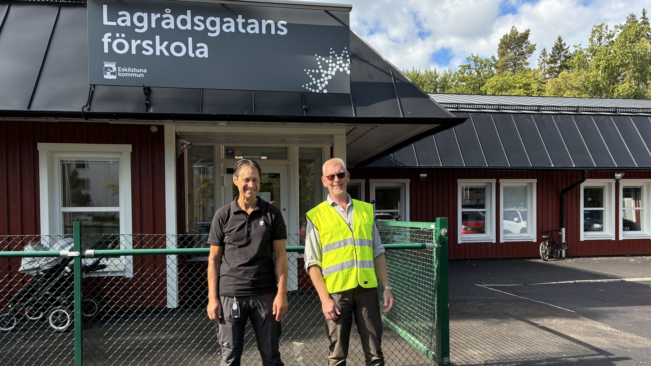 Två personer framför röd förskolebyggnad.